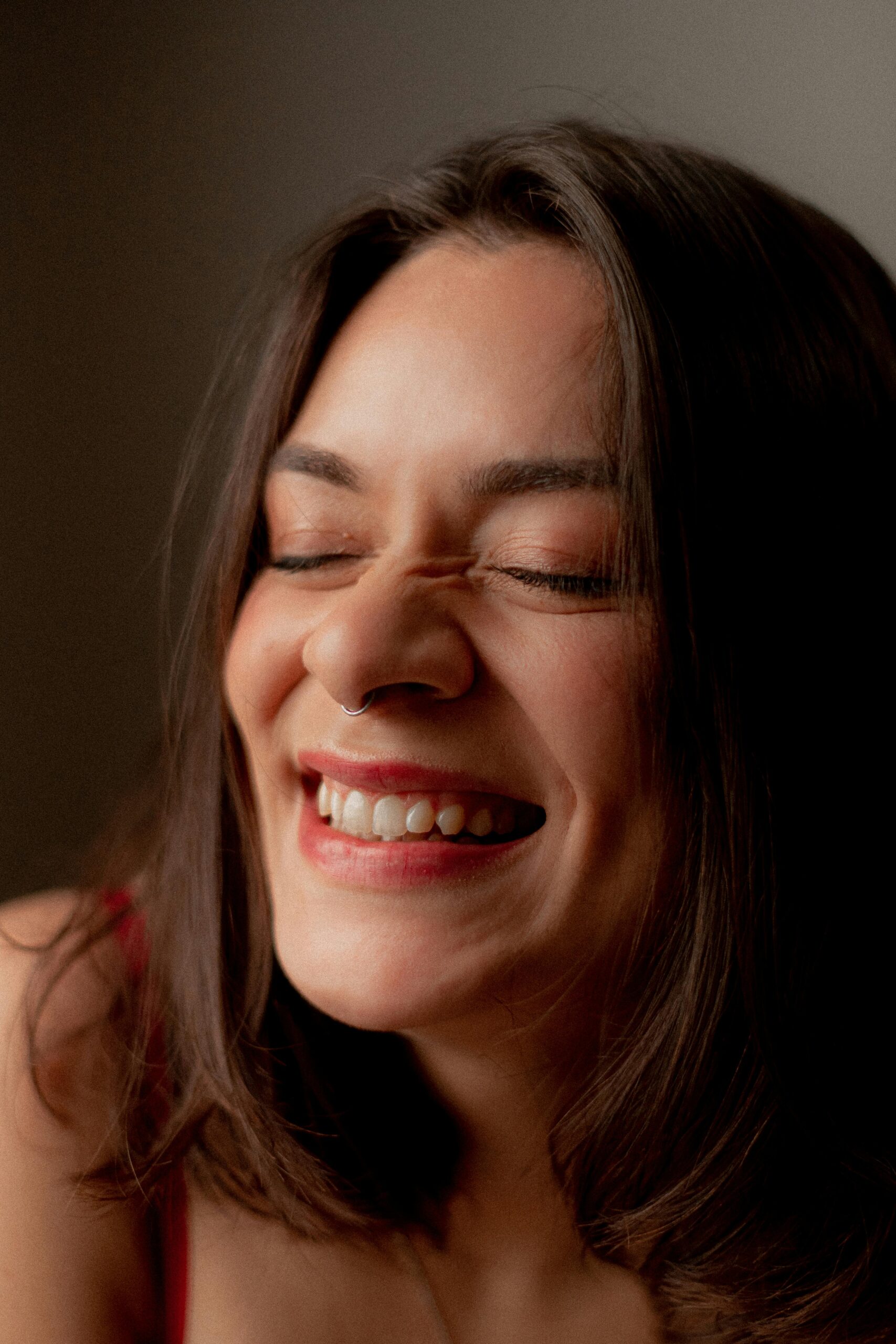 Close-up of a joyful woman with a nose piercing, smiling with eyes closed.
